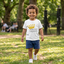 Load image into Gallery viewer, Child wearing a white t-shirt with a crown design and text, standing in a park.