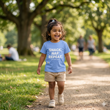 Load image into Gallery viewer, Child wearing a blue shirt with 'SNACK. NAP. REPEAT.' text in a park setting